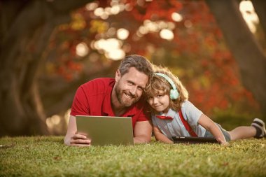 Mutlu çocuk kulaklıkla müzik dinler. Webinar video dersi. Bilgisayarda online eğitim. Özel ders. Baba ve oğul parkta modern iletişim teknolojisini kullanıyorlar. Aile blogu. çocukluk ve ebeveynlik.