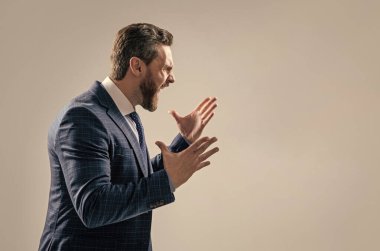 Üzücü bir deneyim. Kızgın patron geniş bir hareket yaparak çığlık atıyor. Çığlık atan işadamı gri arka planda duruyor. Profesyonel adam öfkeyle bağırıyor, boşluğu kopyalıyor..