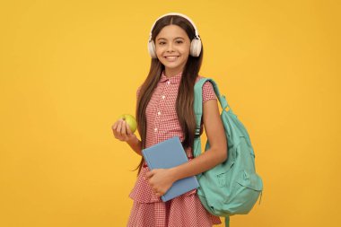 Eğitim konsepti. Öğlen yemeğinde iş kitabı ve elmalı kulaklıklı çocuk. 1 Eylül, sağlıklı bir çocukluk. Okul çantalı çocuk. Müzik. Mutlu genç kız sırt çantası taşıyor. Okula dönüyorum. bilgi günü.