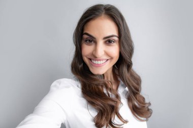 Gülümseyen neşeli kadın gri arka planda cep telefonuyla selfie çekiyor.