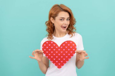 Neşeli kızıl saçlı bayan mavi arka planda kırmızı kalbi tut..