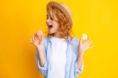 Sarı arka planda lezzetli badem kurabiyesi yiyen genç bir kadın. Kızım, makaronu ye.