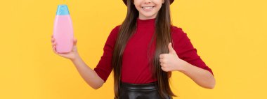 Başparmağını kaldır. Şapkalı mutlu kız şampuanı tutuyor. Gençler için kozmetik ürünler sunuyorum. Çocuk duş jeli kullanıyor. Kuaförde uzun saç şampuanı. Saç kremi kullanan bir çocuk. Günlük alışkanlıklar ve kişisel bakım.