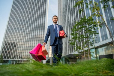 Hediyeli kutusu olan yakışıklı bir adam. CEO doğum günü hediyesi taşıyor. Adam alışveriş torbalarını tutuyor. Erkekler günü. Paketleri olan mutlu bir iş adamı. Satış ve indirim. Ona sürpriz yapacağım. Sevgilim olur musun? Boks günü.