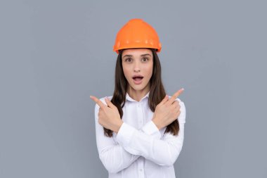 Mimar kadın kaskını gri arka planda takıyor, parmağıyla işaret ediyor.