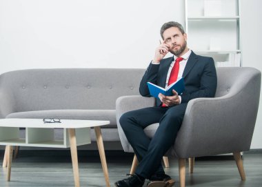 Takım elbiseli, düşünceli, olgun bir iş adamı planlamacıyla ofiste oturuyor..