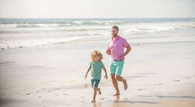 Baba ve çocuk dışarıda eğleniyorlar. Çocukluk ve ebeveynlik. Baba oğul kumsalda koşuyor. Aile seyahati ve tatil. Babalar ya da aile günü. Baba ve çocuk yaz günü.