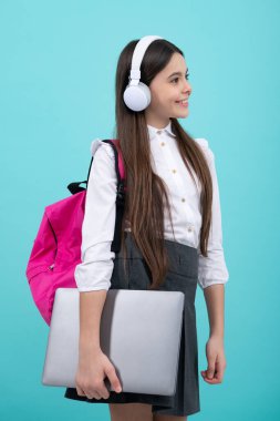 Okula dönelim. Okul üniformalı, çantalı, kulaklıklı ve dizüstü bilgisayarı olan bir kız öğrenci. İzole edilmiş mavi arka planda okul çocukları