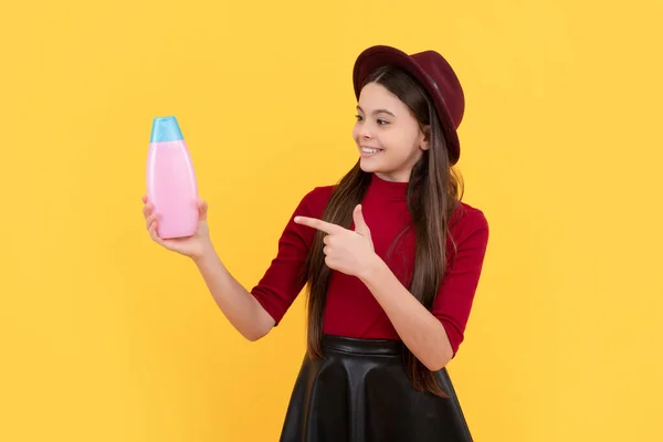 daily habits and personal care. happy girl in hat point finger on shampoo. presenting cosmetic product for teen. kid use shower gel. shampooing long hair in salon. child with conditioner.