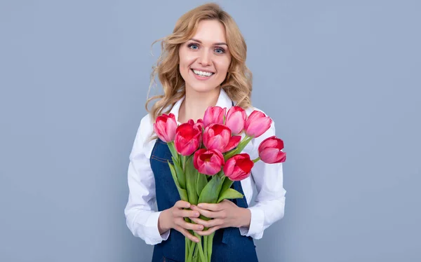 cheerful flower seller woman in apron with spring tulip flowers on grey background.