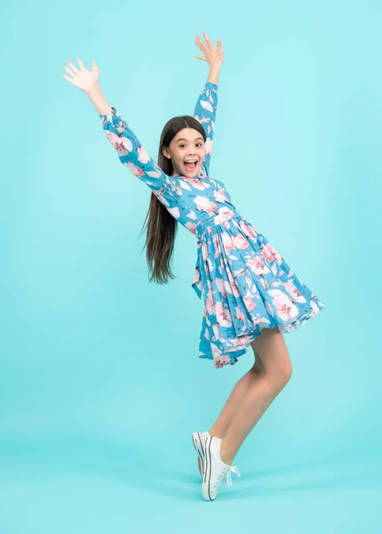 Excited teenager, amazed and cheerful emotions. Happiness, freedom, motion and child. Young teenager girl wear summer dress jumping in air over blue background