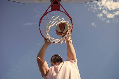 Profesyonel basketbolcu dışarıda antrenman yapıyor. Adamın spor motivasyonu var. Spor ve hobi. Arka planda potada smaç. Smaç basıldı. Yaz etkinliği. Basketbol topu olan adam sahada..
