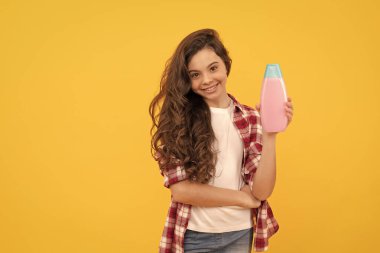 Uzun kıvırcık saçlı mutlu genç kız şampuan şişesi, saç bakımı.