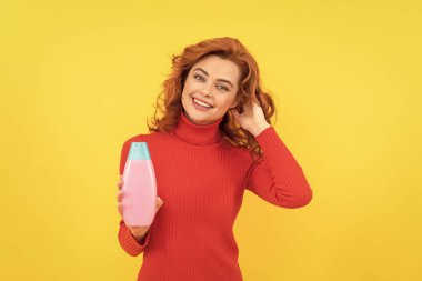 Mutlu kadın duş jeli kullanır. pozitif kız kıvırcık saçlı şampuan şişesi tutuyor. Saç kremi reklamı. Güzellik ürünü. Günlük alışkanlıklar ve kişisel bakım. Kızıl saçlı kadın kozmetik ürünleri sunuyor..