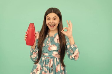 Şaşırmış uzun saçlı çocuk şampuan şişesi tutuyor. Tamam jest yap, reklam yap..