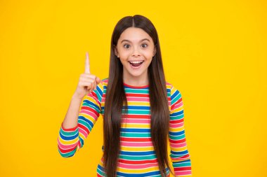 Mutlu yüz, pozitif ve gülümseyen genç kız duyguları. Sarı arka planda izole edilmiş, parmağıyla işaret eden genç bir kızın portresi. Kızın harika yeni bir fikri var. Başarılı çocuk.