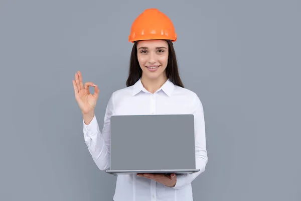 Young woman construction manager. Woman builder isolated portrait with protect helmet and laptop computer. Gray background, copy space