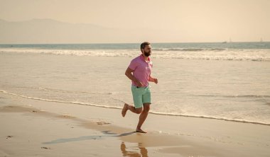 Mutlu koşucu adam yaz plajında yalınayak koşuyor..