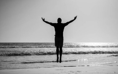 Yaz plajında zıplayan atletik bir adamın silüeti, özgürlük..