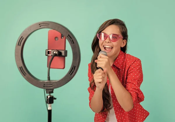 快乐的Vlogger与麦克风 在智能手机上制作视频博客 博客灯笼 网上声乐辅导课 少年女歌手用自拍为领唱 儿童音乐博客 卡拉Ok 孩子在唱歌 — 图库照片