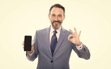 Reklam sunumu. kopyalama alanı. Boz adam telefon ekranını sunuyor. Yetişkin bir iş adamı beyaz telefondan izole edilmiş akıllı telefon gösteriyor. Takım elbiseli bir adam. Yeni uygulama. Tamam jest. ürün önerisi.
