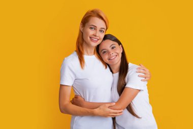 Anne ve kız tişörtlü çocuk sarı arka plan stüdyosunda izole edilmiş Cudding 'i kucaklıyor. Anneler günü aileyi sever.