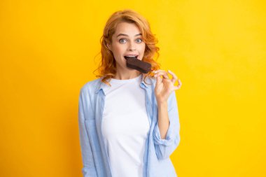 Sarı arka planda çikolatalı dondurmalı kızıl saçlı kızın portresi. Dondurma yiyen kıvırcık, neşeli kadın.