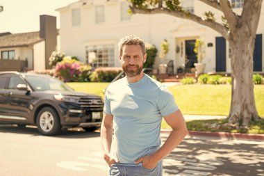 smiling dealer man standing next to the car and new house.