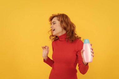 Mutlu kızıl saçlı, kıvırcık saçlı, saç boyalı, şampuanın vücut bakımını sunan eğlenceli, kozmetik ürünleri..