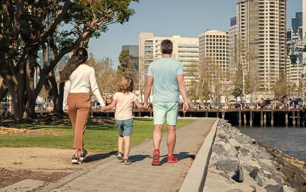 young family walking in park with son back view, parents.