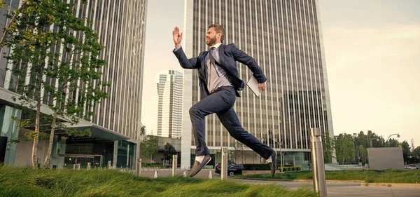 successful man in formalwear jumping with computer outside the office, technology.