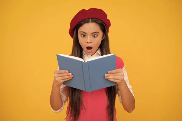 surprised teen school girl in french beret reading book on yellow background, surprise.