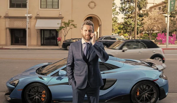 businessman talk on phone next to luxury car.