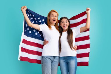 Heyecanlı anne ve çocuk Amerikan bayrağı taşıyor. Vatansever bayram. Mutlu aile, mavi izole edilmiş stüdyo geçmişinde Amerikan bayrağı taşıyan anne ve kızı. ABD 4 Temmuz 'da bağımsızlığını kutladı