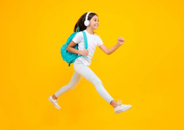 Okul boş vakitlerinde. Mutlu ergen portresi. İzole edilmiş stüdyo geçmişi olan kulaklıklı bir kız öğrenci. Okul ve müzik konsepti. Atla ve kaç, zıplayan çocuk.