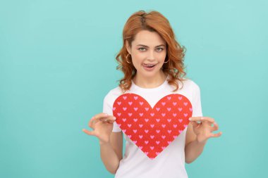 Gülümseyen kızıl saçlı kadın mavi arka planda kırmızı kalbi tut..