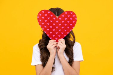 Neşeli romantik genç kız sarı arka planda izole edilmiş sevgililer günü için aşkın kırmızı kalp sembolünü taşıyor.