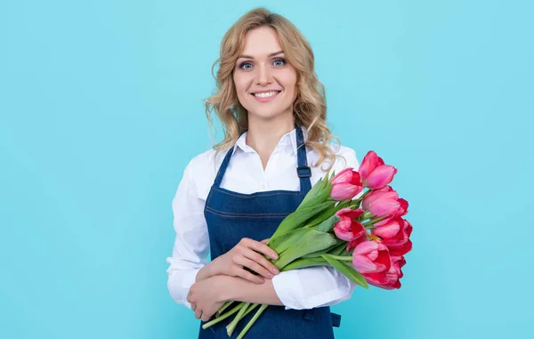 smiling flower seller woman in apron with spring tulip flowers on blue background.