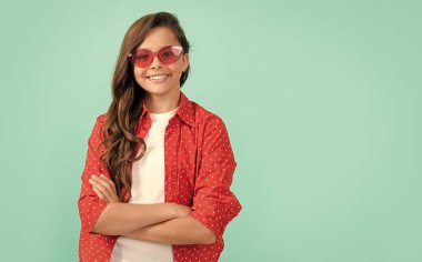 Olumlu duygularını ifade et. Güneş gözlüklü, uzun saçlı, gülümseyen çocuk. Güzellik ve moda. Kadın manken. Genç bir kızın güzel görünüşü. Mavi arkaplanda çocuk portresi.