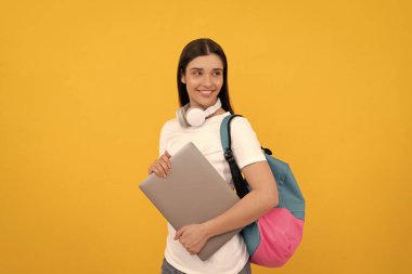 Sırt çantası ve kulaklığı olan gülümseyen kız. Modern eğitim için webinar. İletişim teknolojisi. Okul çantalı bir kadın dizüstü bilgisayar tutuyor. İnternetten al. Okula dönüyorum. Etkilendirici günlüğü.