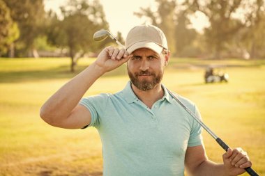 Profesyonel golf sahasında erkek golfçü. Golf sopasıyla şapkalı golfçünün portresi. İnsanların yaşam tarzı. Yeşil çimlerin üzerinde yakışıklı bir adam. Yaz etkinliği. Profesyonel spor..