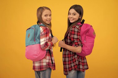 1 Eylül. Mutlu çocukluk. Okul çantalı çocuklar. Dost canlısı genç kızlar sırt çantası taşır. Okula dönüyorum. Bilgi günü. Eğitim konsepti. Sarı arka planda uzun saçlı çocuklar..