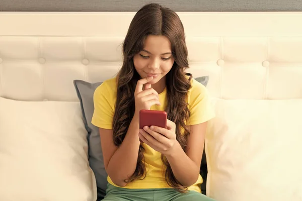 快乐的女孩坐在床上聊天 一边用手机聊天 一边笑着 — 图库照片