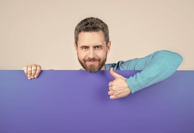 Boş mavi kağıt pankartın arkasında sunum için fotokopi alanı olan neşeli, olgun, sakallı adam baş parmağını kaldır ve iletişim kur..
