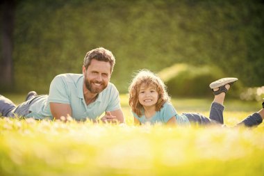 Çocukluk ve ebeveynlik. Ebeveyn, küçük çocuk çimlerin üstündeyken rahatlar. İyi ki babası yaz günü çocuklu. Ebeveynlik ve babalık. Babalar günü. Mutlu baba ve oğul parkta eğleniyor. aile değeri.