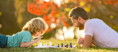 Baba oğul açık havada satranç oynar, afiş afişi yapıştırır, babalar günü olur. Mutlu bir aile. Ebeveynlik ve çocukluk. şah mat
