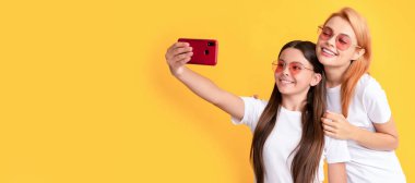 Anne ve kız çocuk afişi, kopyalama alanı, izole edilmiş arka plan. Anne ve çocuk blogcuları. Güzel kadın ve kız akıllı telefonla selfie çekiyorlar. Selfie ailesi