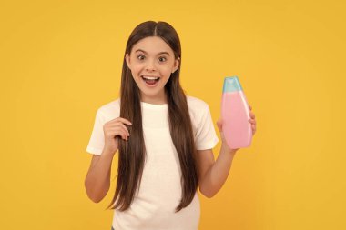 Çocuk duş jeli kullanıyor. Kuaförde uzun saç şampuanı. Saç kremi kullanan bir çocuk. Günlük alışkanlıklar ve kişisel bakım. Vücut bakımı kozmetik. Şaşırmış kız şampuan şişesini tutuyor. Gençler için kozmetik ürün sunumu.