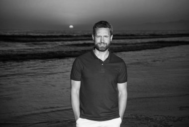 Yaz tatili. pozitif duygular. Gün batımında sakallı gülümseyen bir adam. Sahildeki traşsız adam. Gündoğumu plajındaki beyaz adam. Gömlekli sakallı adam. Yaz modası.