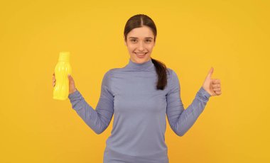 Mutlu genç bir kadın elinde su şişesi, başparmağıyla jest ve sağlık hizmeti yapıyor..